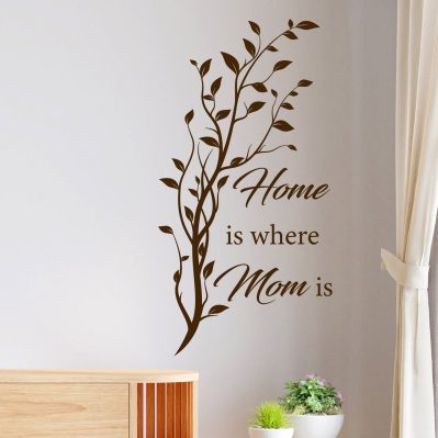 Adesivi parete soggiorno con frase “Home is where Mom is” in vinile marrone su parete chiara, con ramo verticale decorativo.