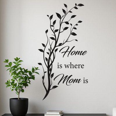 Adesivi parete soggiorno con frase “Home is where Mom is” in vinile nero applicato su muro bianco con design naturale verticale.