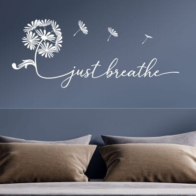 Sticker da parete camera da letto con frase “just breathe” in vinile bianco su parete blu.