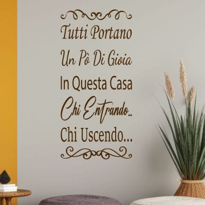 Scritta murale adesiva per la casa con frase accogliente su parete beige con pouf e pianta decorativa
