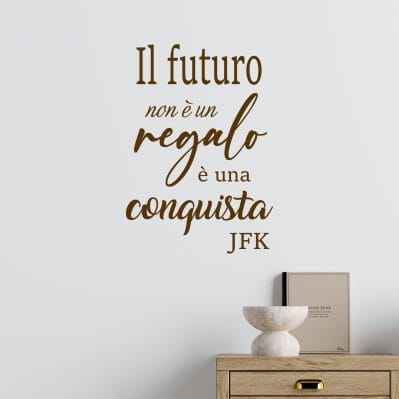 Adesivo da parete citazione motivazionale Il futuro non è un regalo è una conquista JFK in colore marrone applicato su parete chiara sopra mobile in legno moderno.