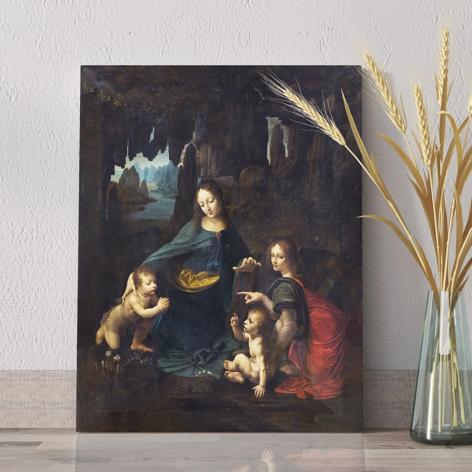 Quadro Vergine delle Rocce Leonardo da Vinci appoggiato su piano chiaro con vaso decorativo.